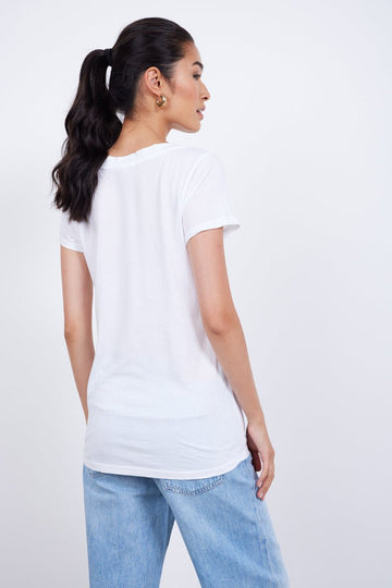 Woman with a ponytail wearing an ethically made LAmade LOW v NECK BOYFRIEND TEE and blue jeans, standing sideways and looking slightly over her shoulder against a white background.